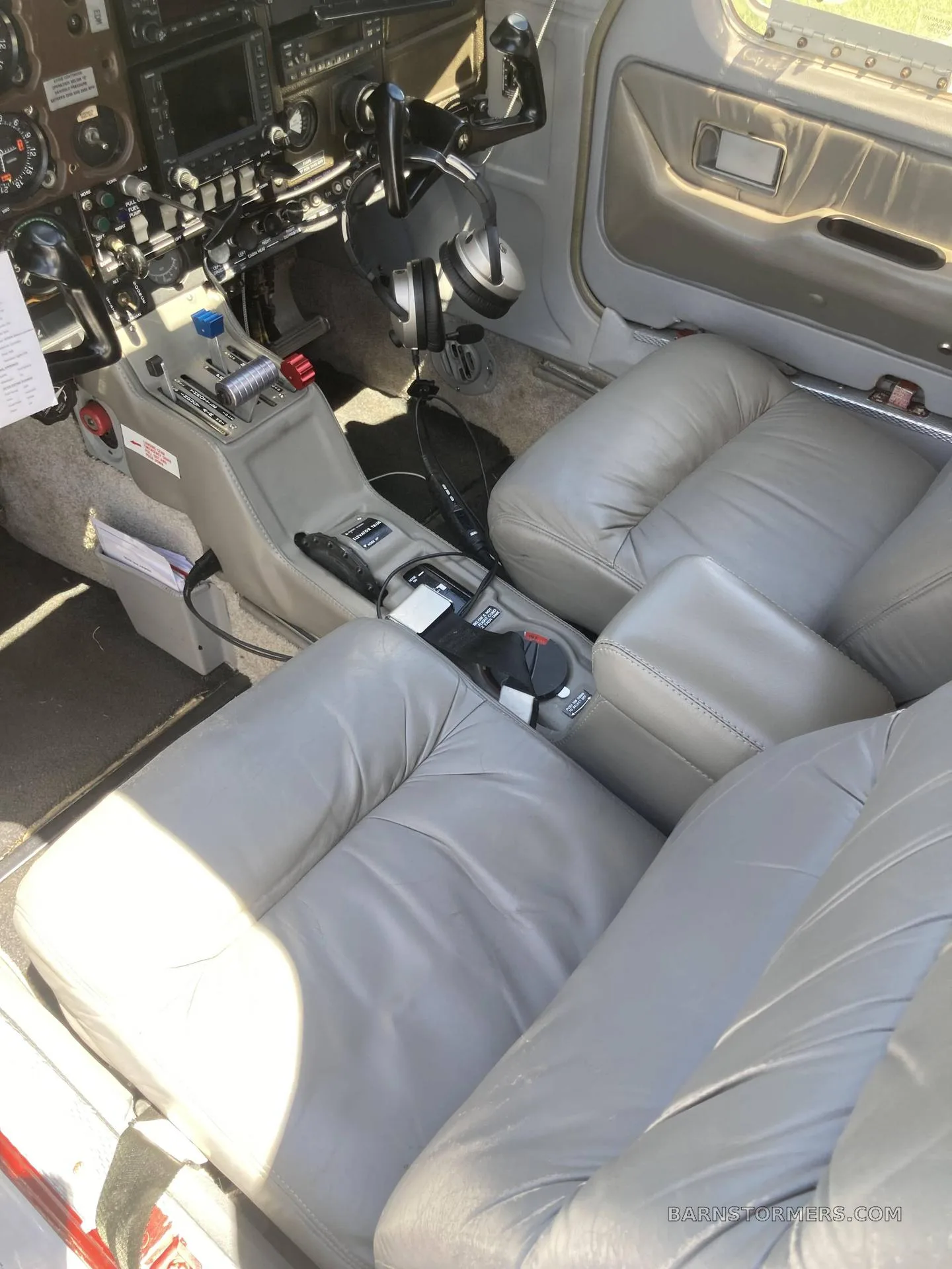 The light gray leather interior of an aircraft cabin, showing the front seats and center console with cockpit controls in the background.