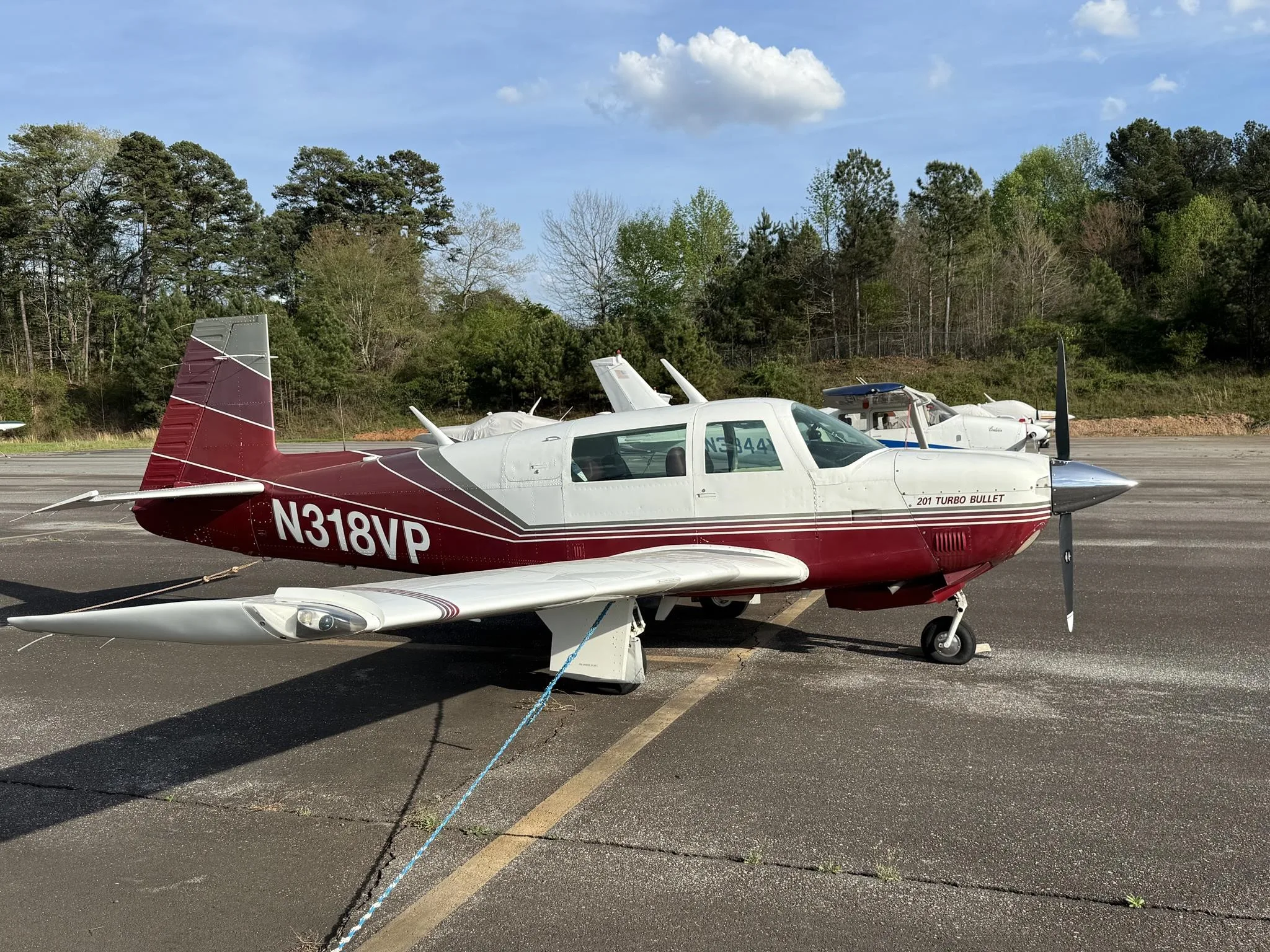 A red and white Mooney 201 Turbo Bullet aircraft, N318VP, parked on an asphalt ramp with trees in the background.