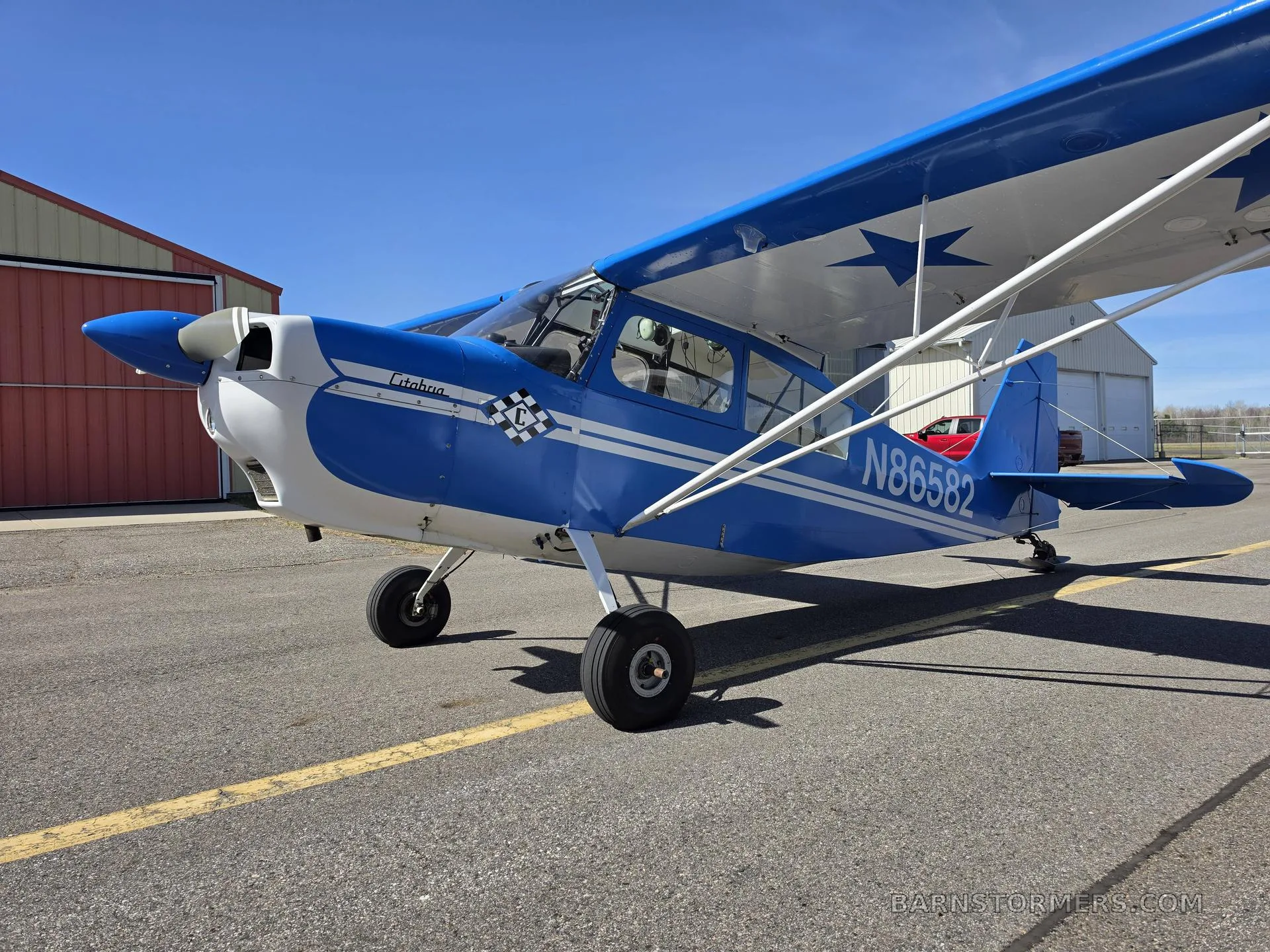 A blue and white single-engine propeller aircraft, tail number N86582, parked on an asphalt ramp with hangars in the background.