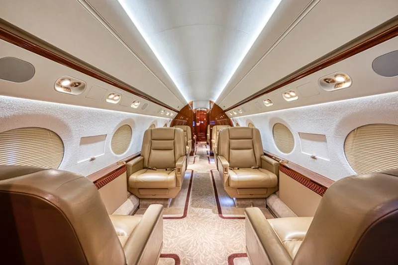 The luxurious cabin interior of a business jet with tan leather seats and a patterned aisle carpet.