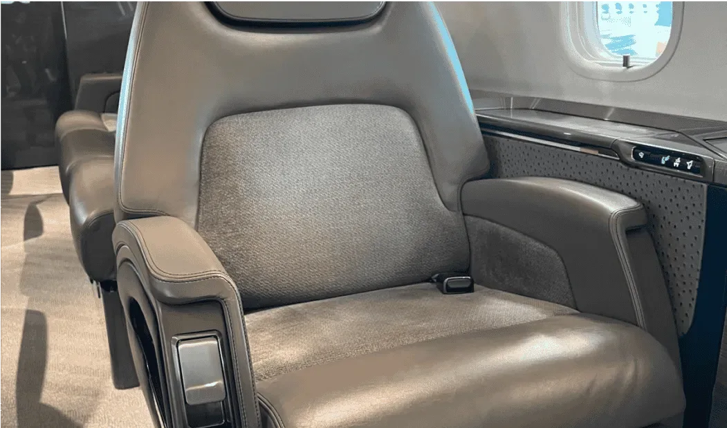 A close-up view of a grey leather aircraft cabin seat with a textured fabric insert.