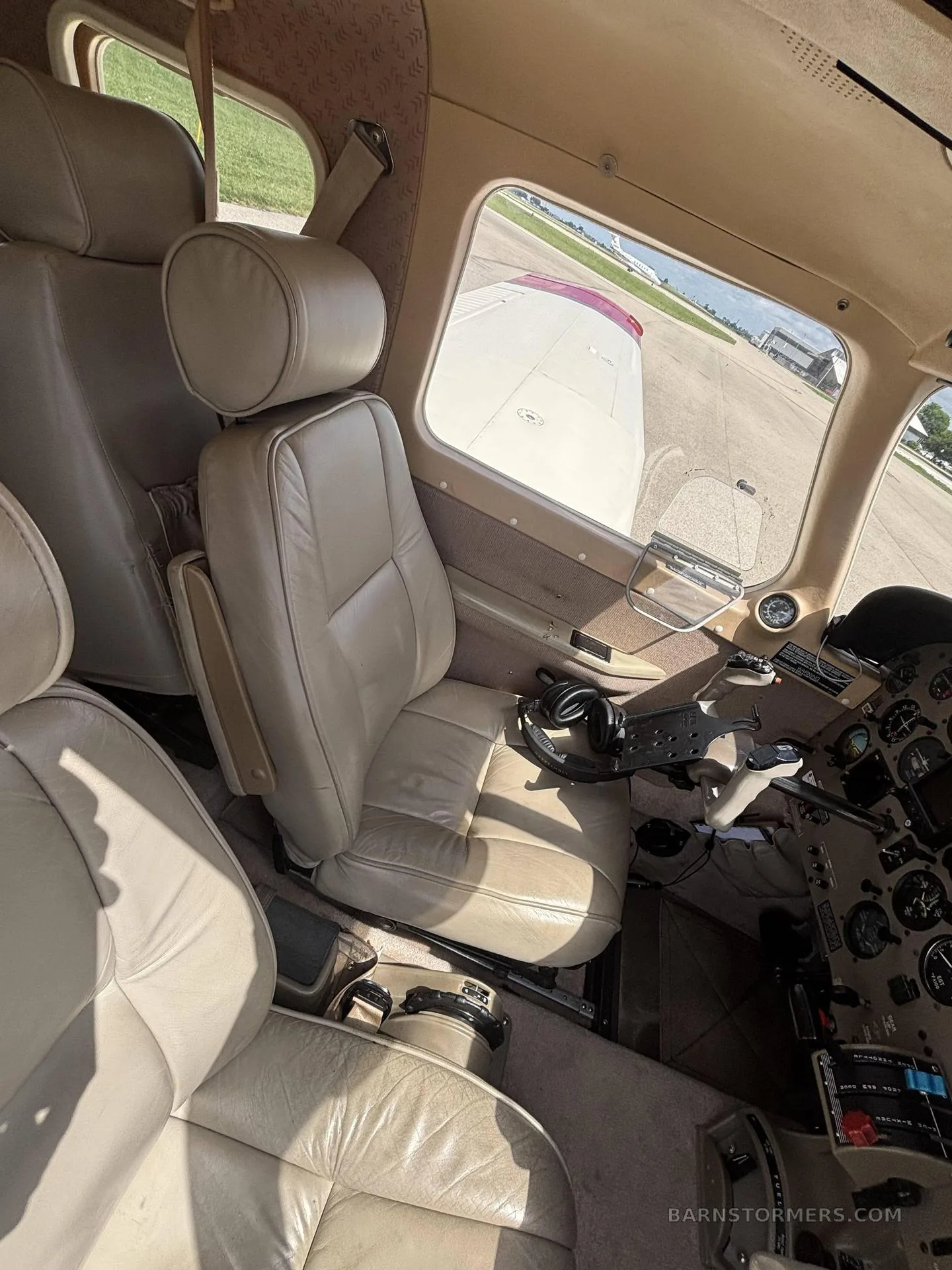The light tan leather interior of a Piper Saratoga II HP, showing the front passenger seats and a view of the wing outside.