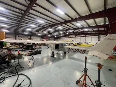 A white Cessna 150/152 type aircraft with registration N10946 is parked in a hangar, viewed from the right rear.