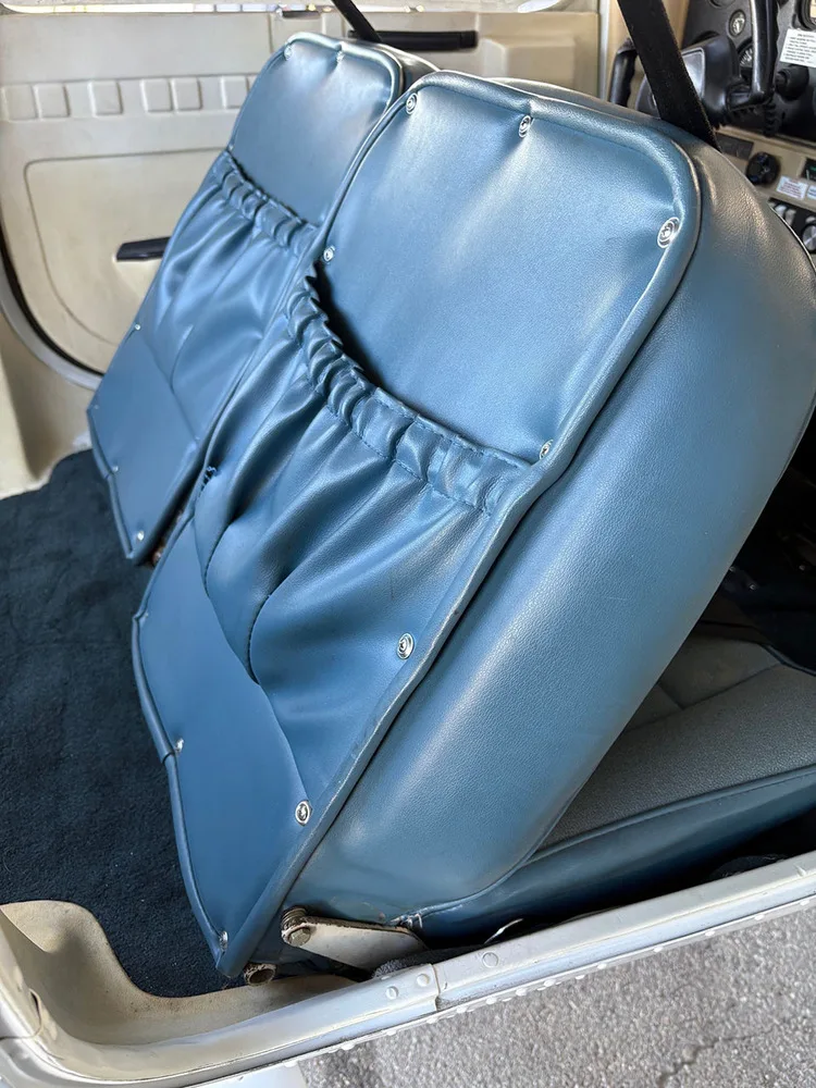 The back of two blue vinyl aircraft seats with storage pockets, looking towards the rear cabin.