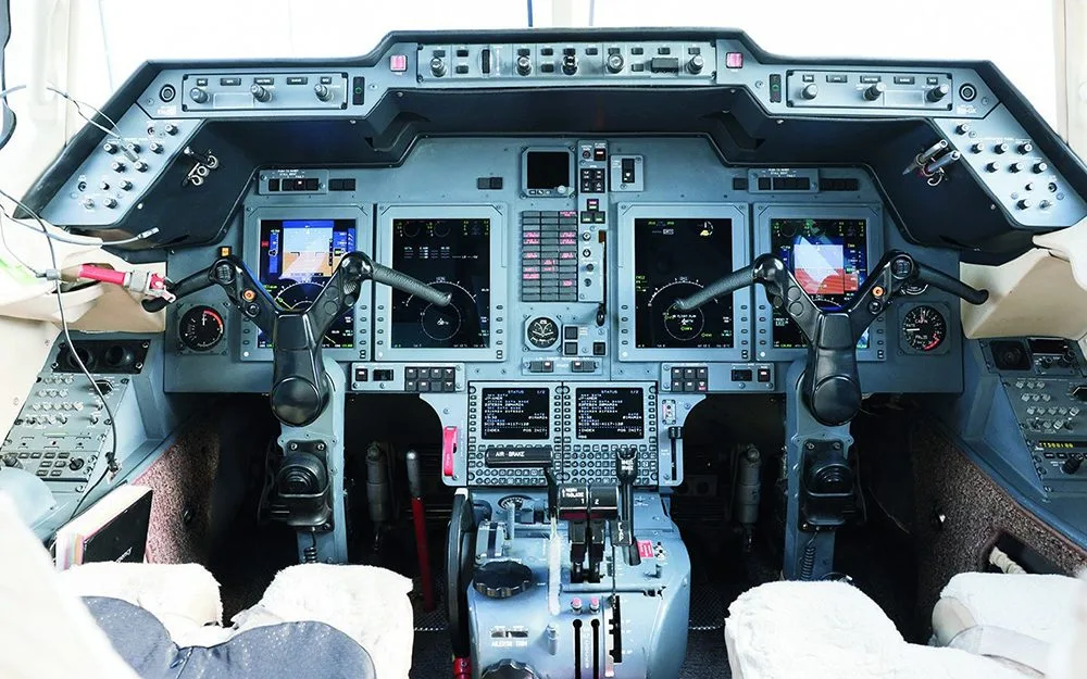 The cockpit of a private jet features multiple digital displays and a complex control panel.