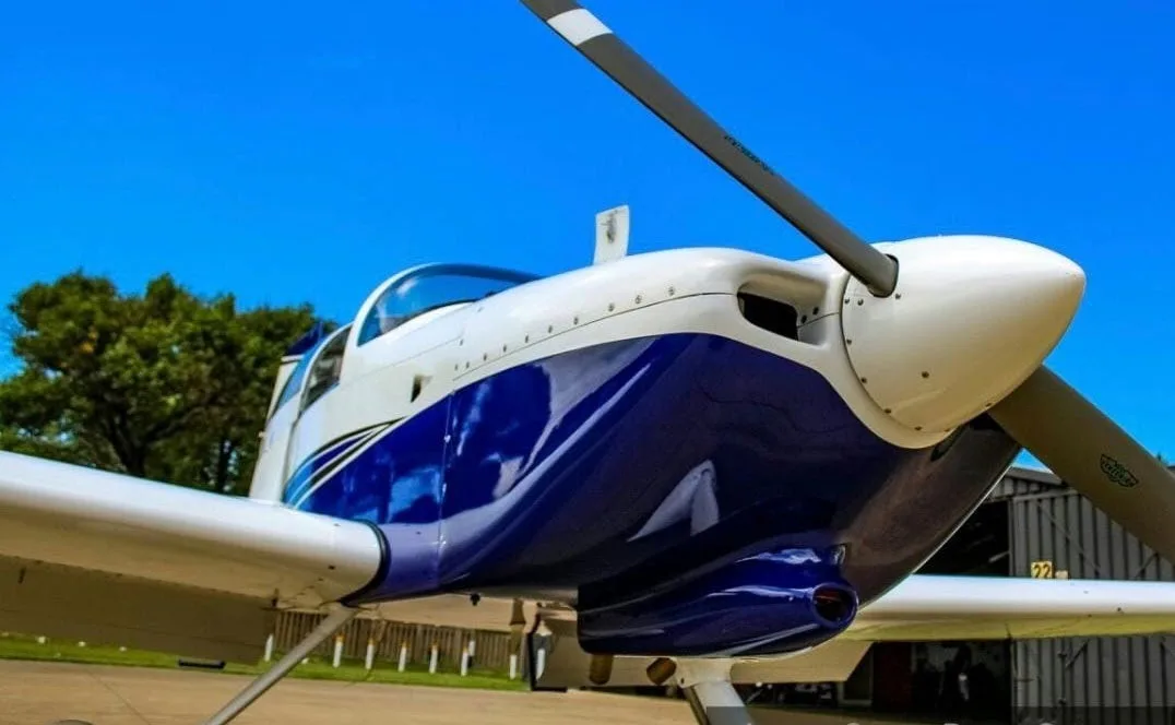 A close-up view of the front of a white and blue single-engine aircraft, showing the propeller and engine cowling against a blue sky.