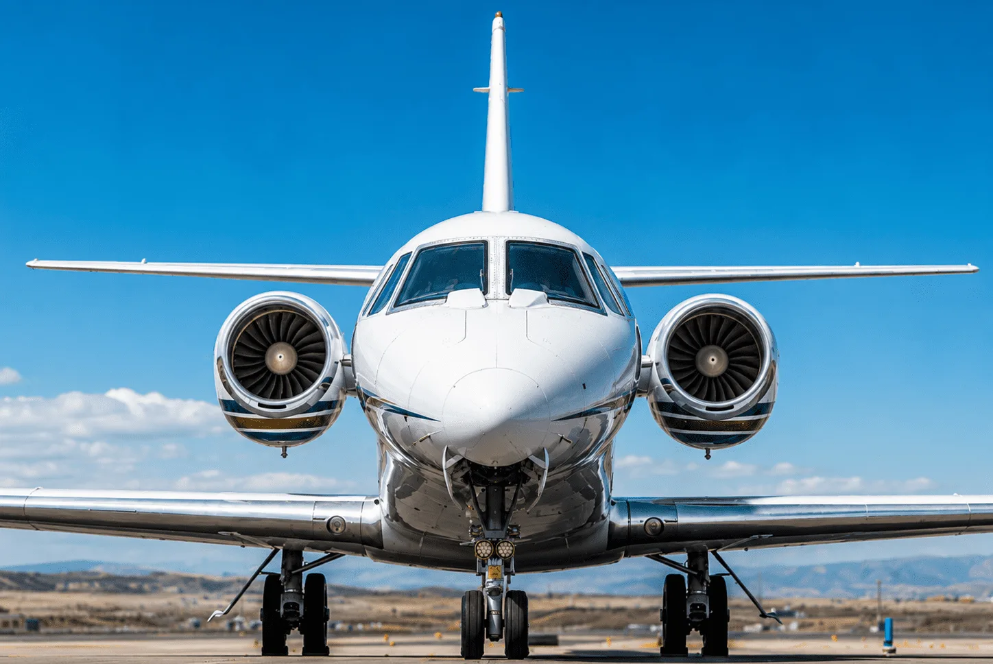 A white business jet with dark accent stripes, viewed head-on on a tarmac under a clear blue sky.
