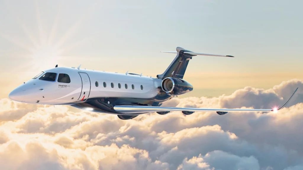 A silver Embraer Phenom 300 in flight above the clouds.