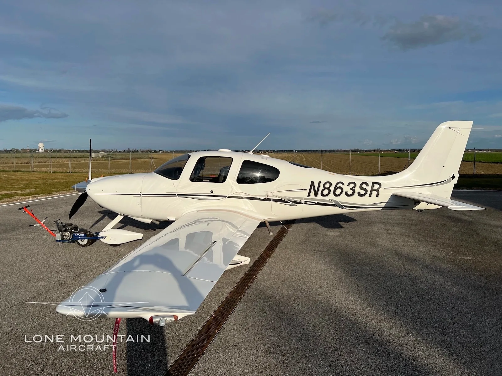 A white Cirrus SR22 aircraft with registration N863SR is parked on an airfield, viewed from the rear-left wing.