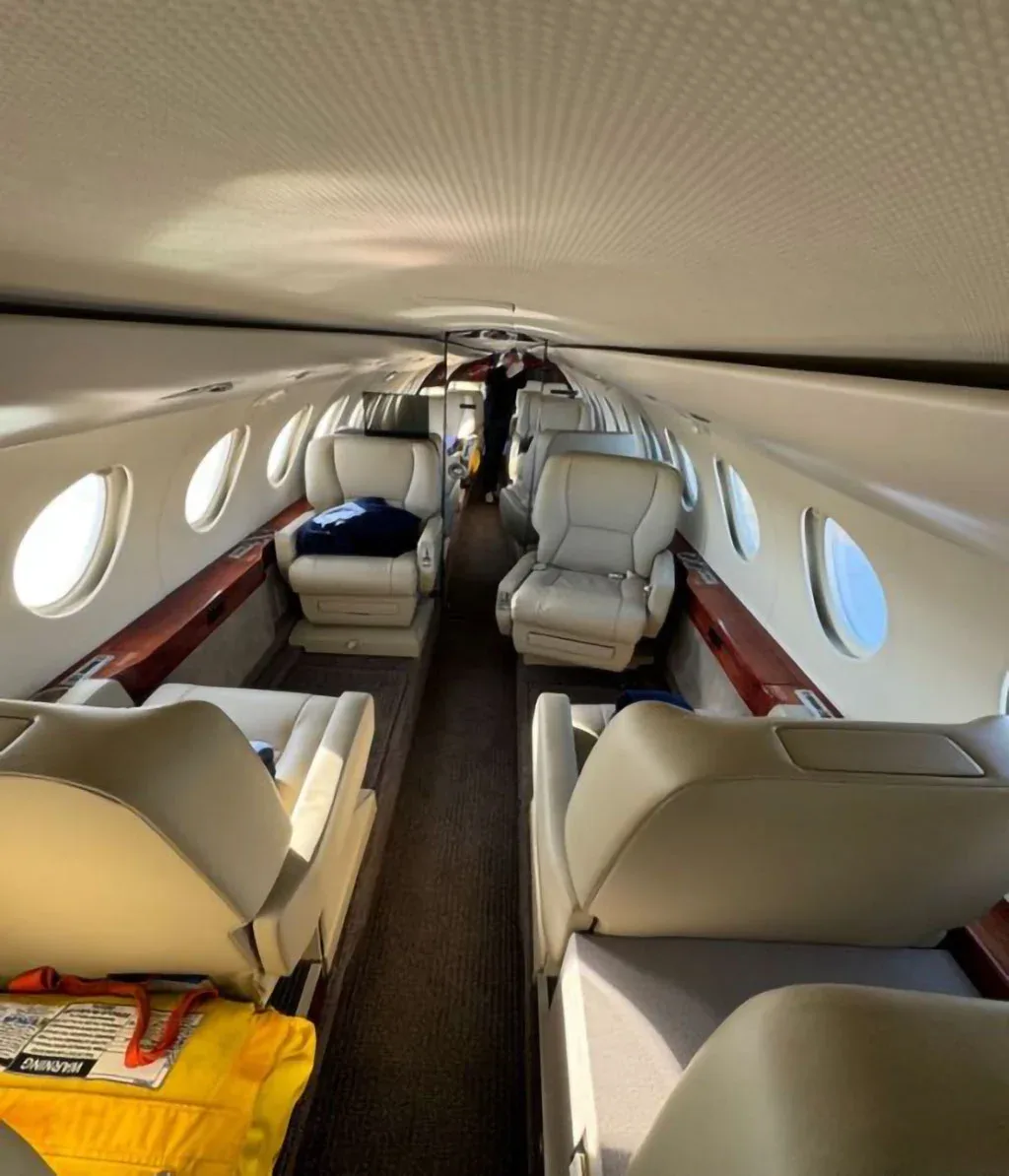 View down the aisle of a private jet cabin with light-colored leather seats.