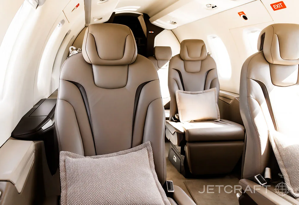 A close-up view of the light brown leather seats in the aircraft cabin, with a small pillow on one seat.