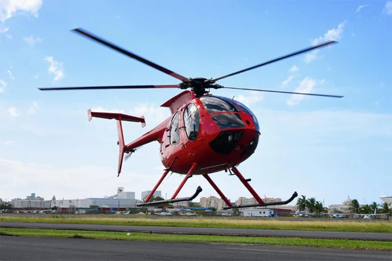A red helicopter is shown on the runway with its blades spinning.