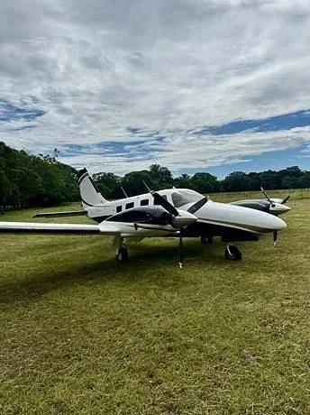 A white and black twin-engine propeller aircraft is parked on a grassy field under a cloudy sky.