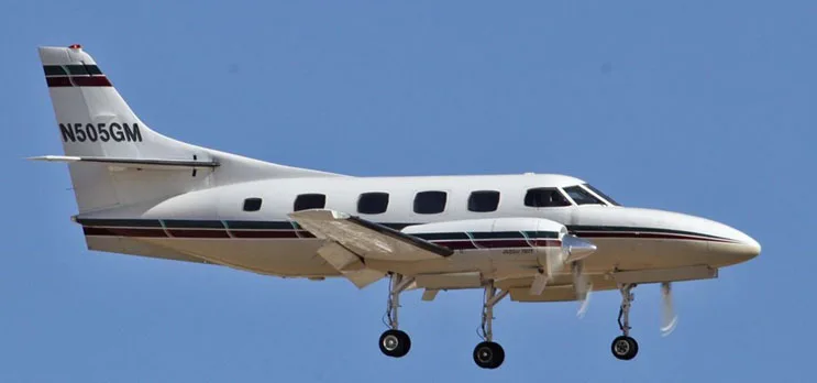 A white twin-engine turboprop aircraft, registration N505GM, flying with landing gear extended against a blue sky.