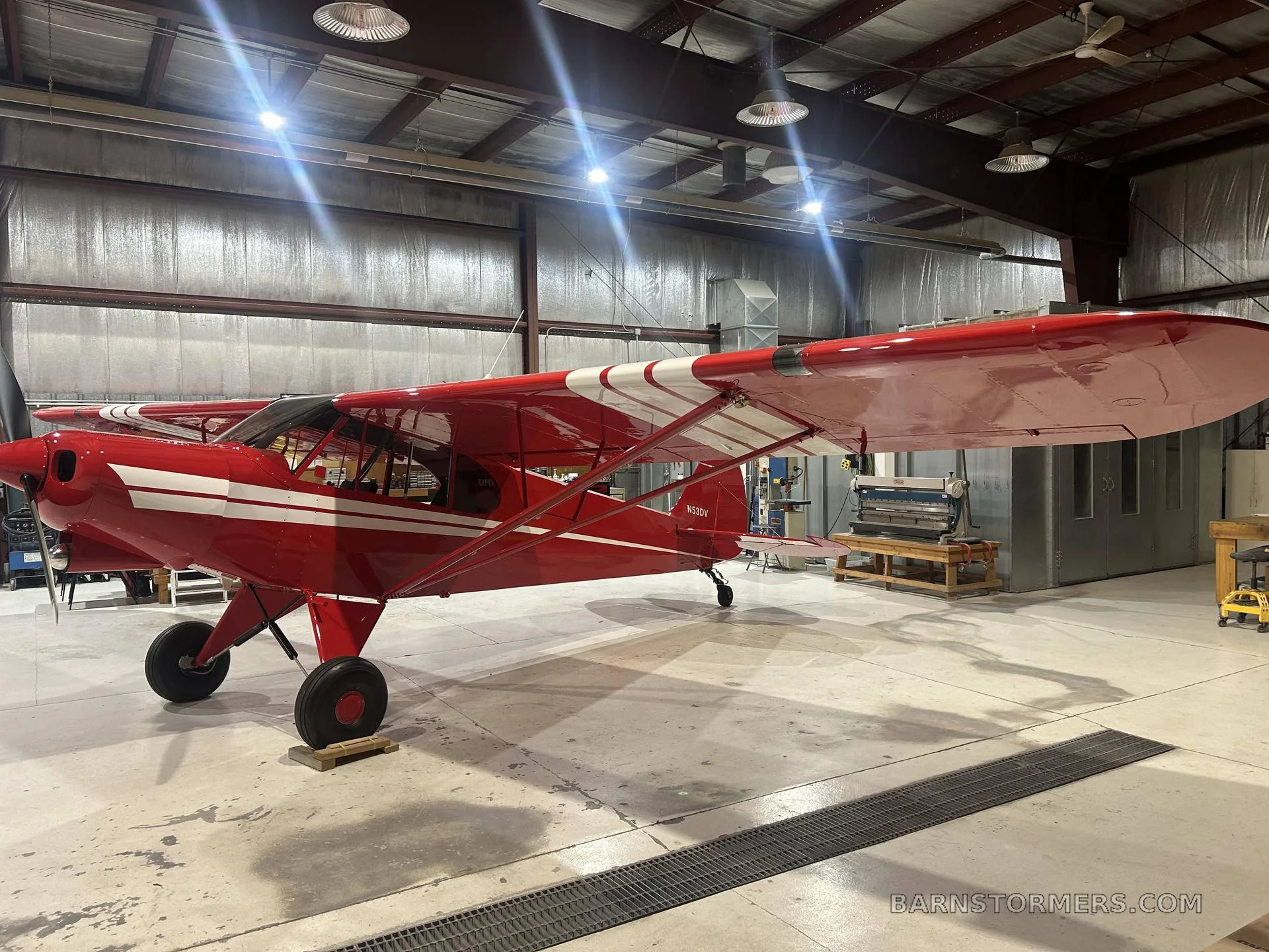 A red PA-18 Supercub parked inside a hangar.