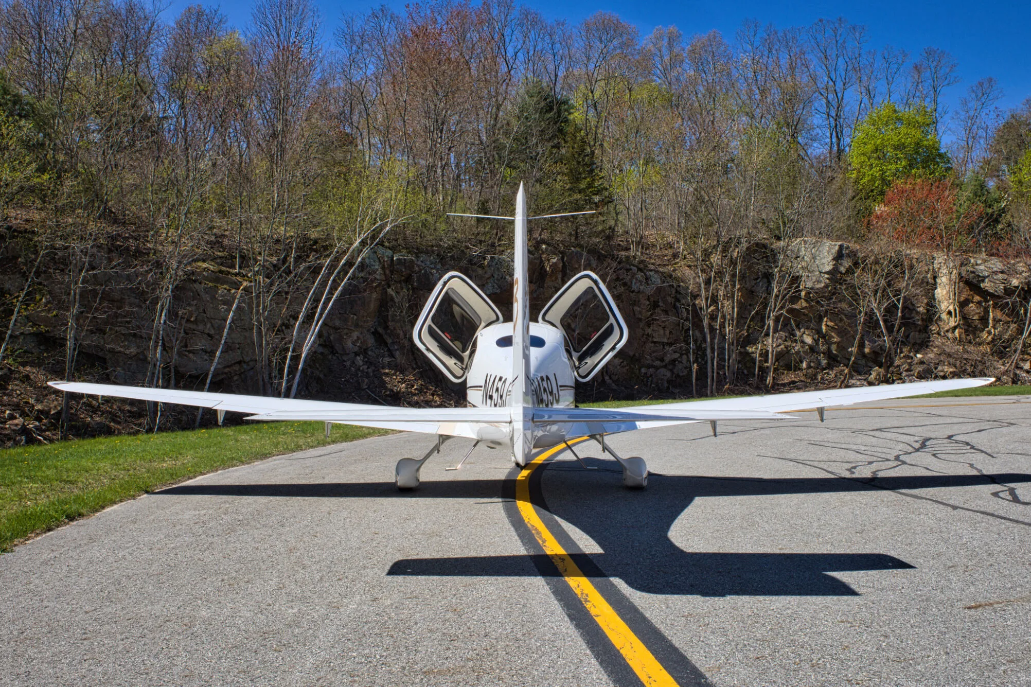 A rear view of the white Cirrus SR22 GTS Generation Three aircraft (N459J) with both gull-wing doors open, parked on an airfield.