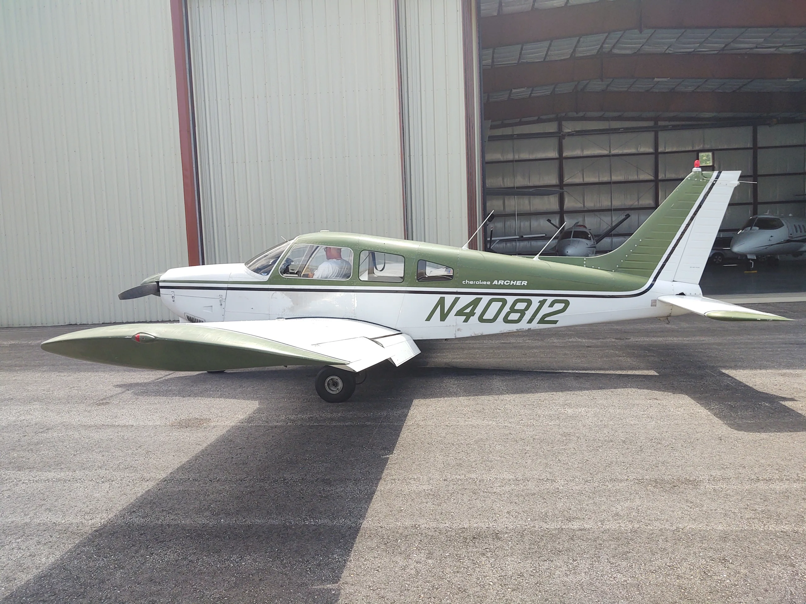 A white and green Piper Cherokee Archer aircraft with registration N40812 parked on an asphalt ramp outside a hangar.