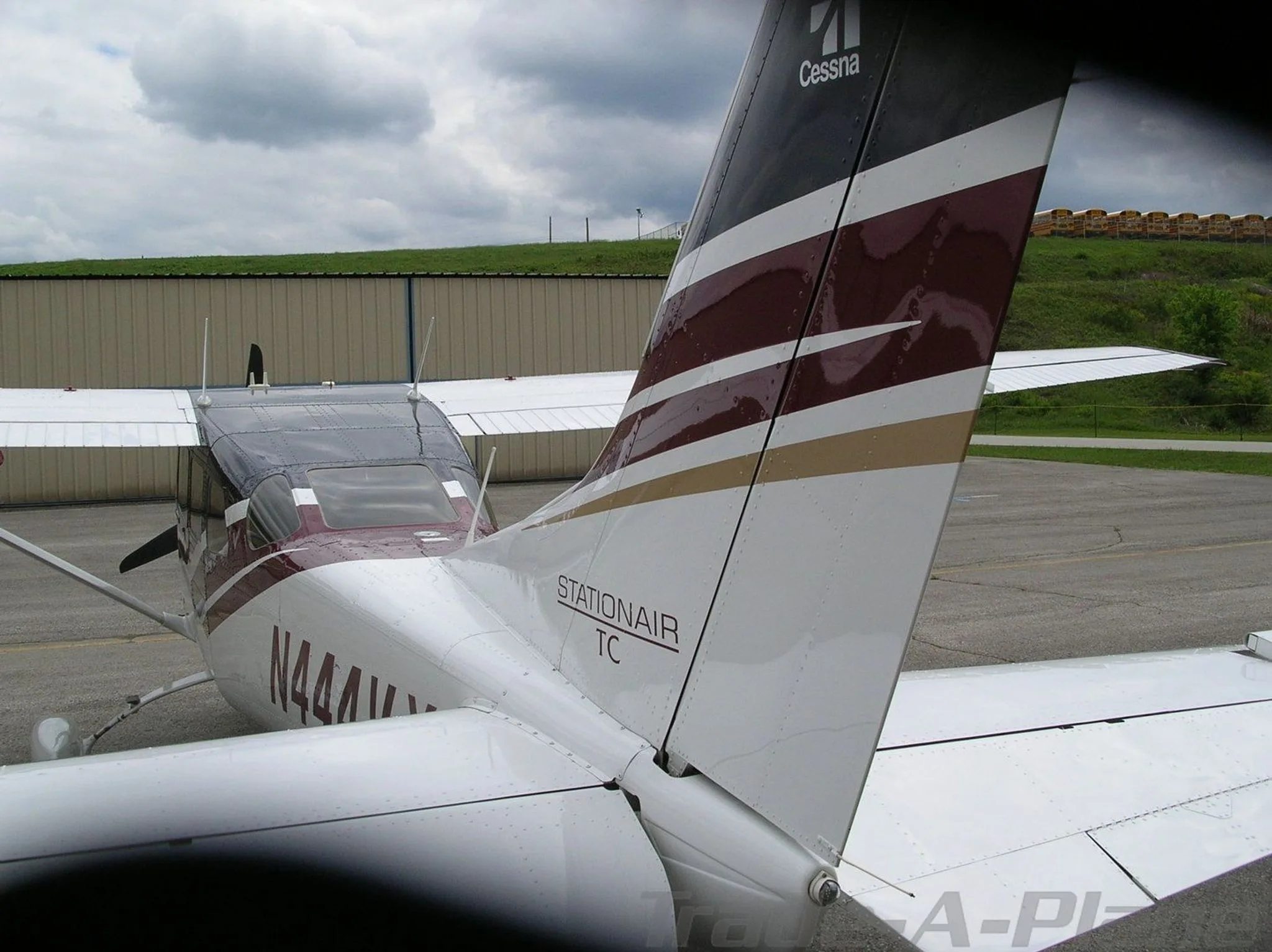 A rear view of the tail of a white Cessna Stationair TC with dark blue and maroon stripes, registration N444VX, parked on an asphalt ramp.