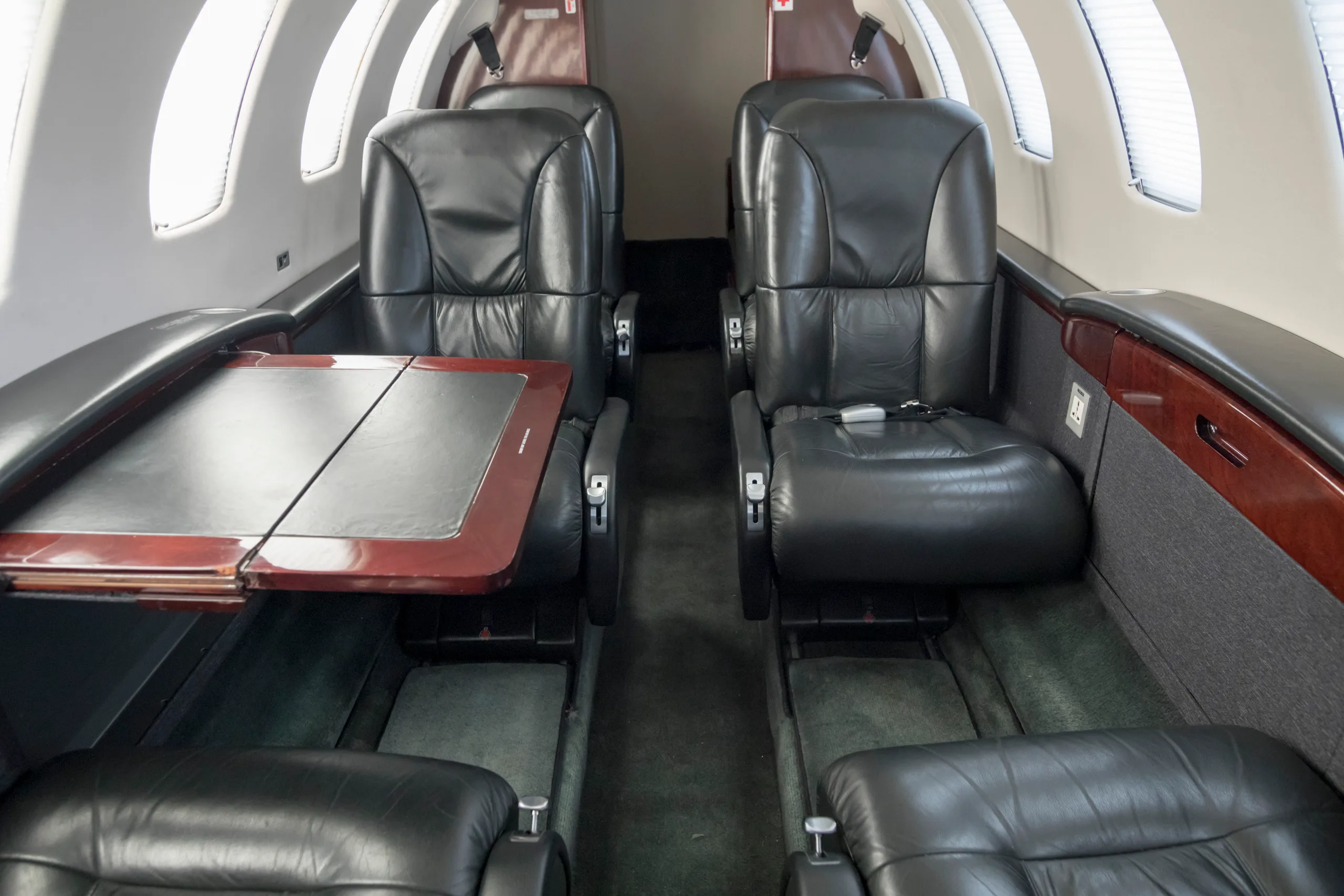 The interior cabin of a private jet with black leather seats facing each other and a fold-out table.