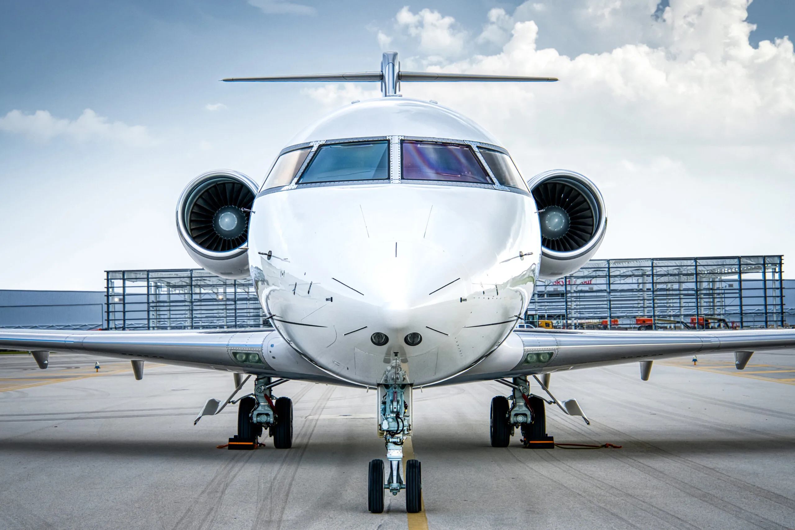 A front view of a white Bombardier Challenger business jet with gold and black stripes, registration LV-KKF, parked on an airport tarmac.