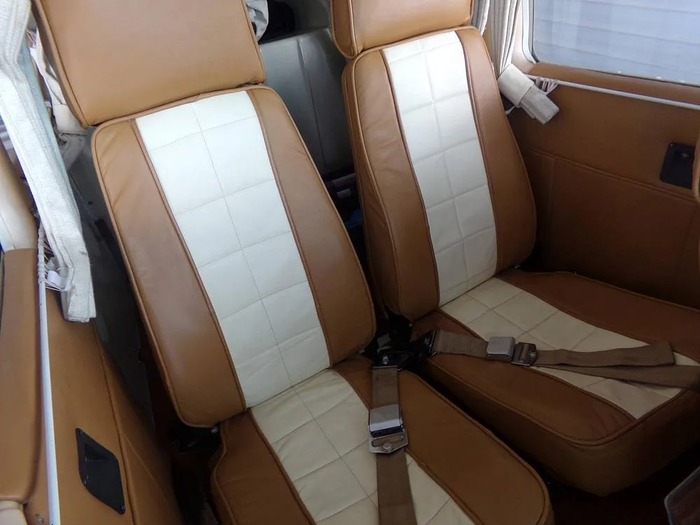 A close-up view of two tan and white leather aircraft seats with seatbelts in the cabin.