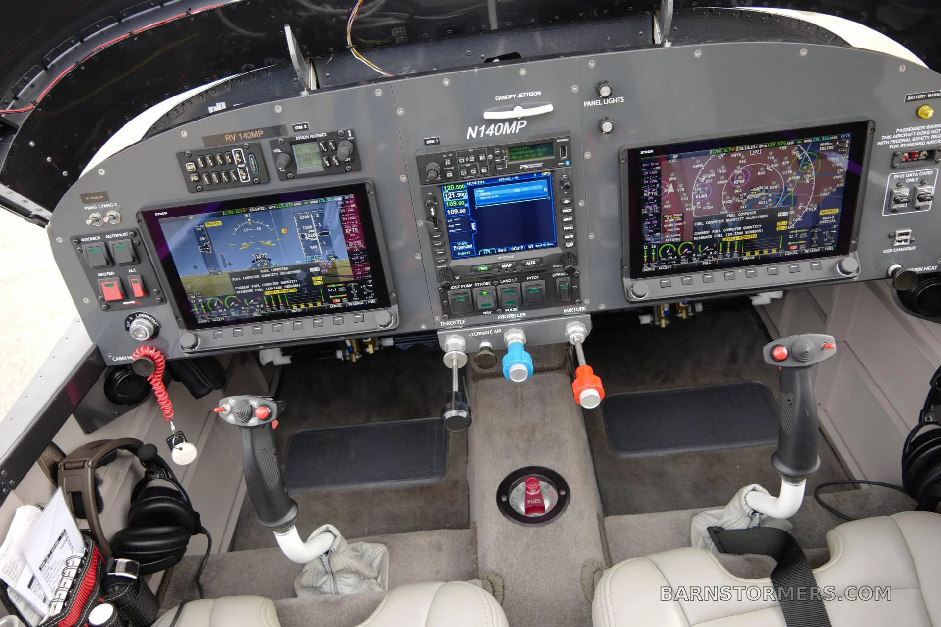 The cockpit of a Vans RV-140MP aircraft, featuring three large digital displays, control sticks, and a throttle quadrant.