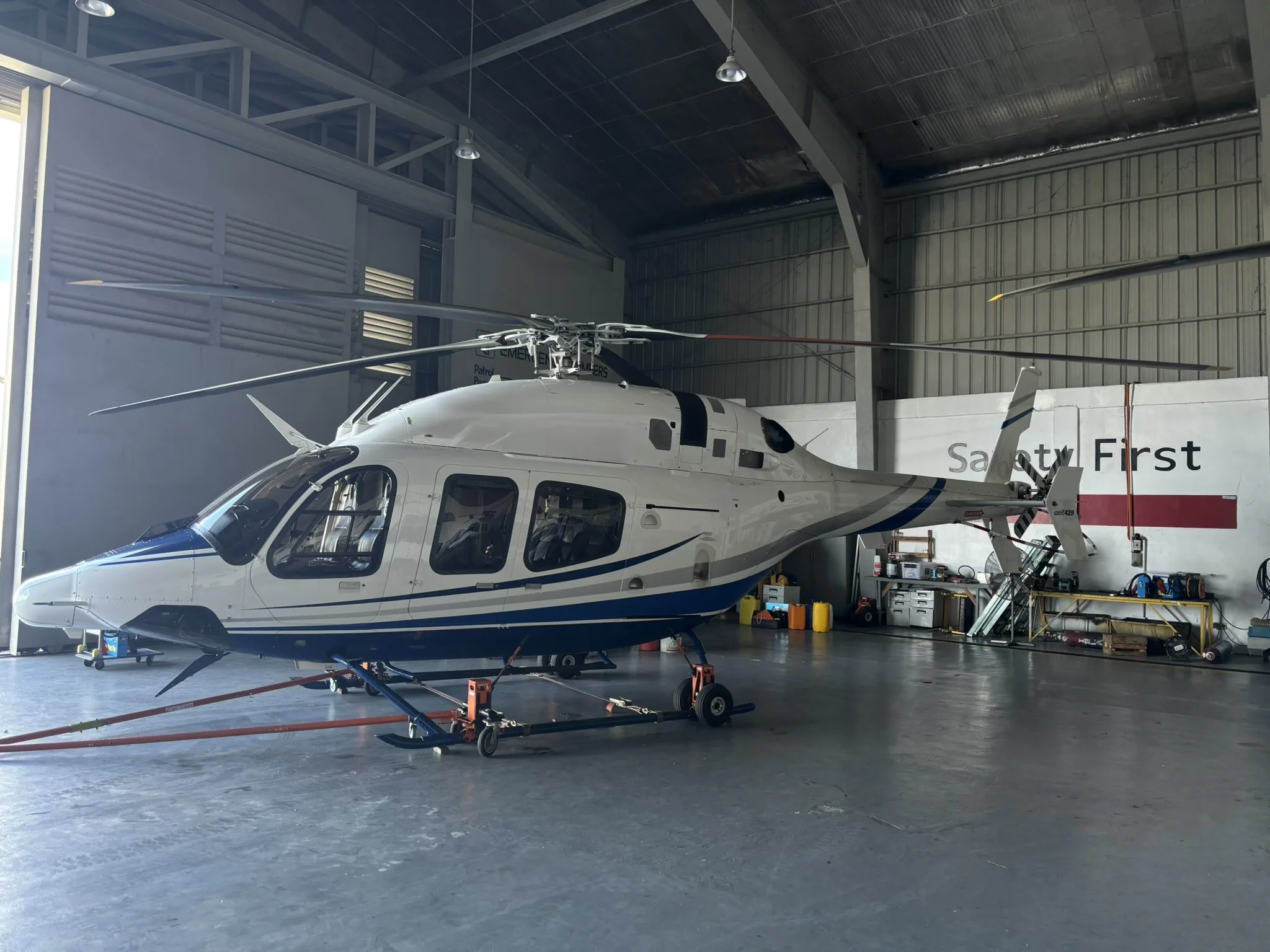 A white and blue Bell 429 helicopter is parked inside a hangar.