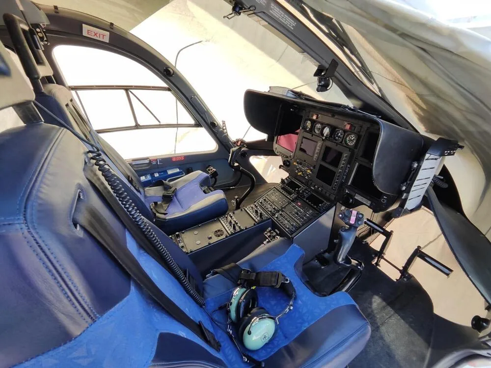 The cockpit of a helicopter features blue seats, a detailed instrument panel, and flight controls.