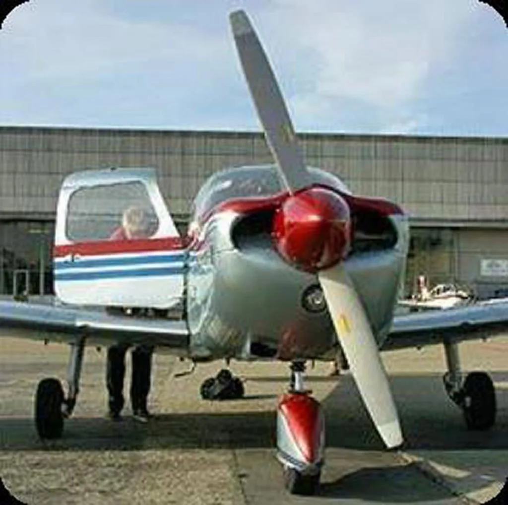 Front view of a red and silver single-engine propeller aircraft with an open door, showing a person inside.