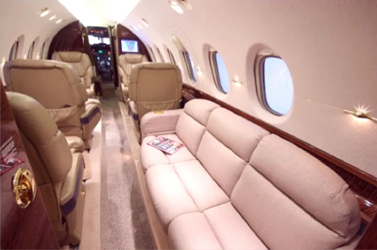 A long view of the aircraft cabin showing a beige sofa on the right and multiple tan leather seats further down the aisle.