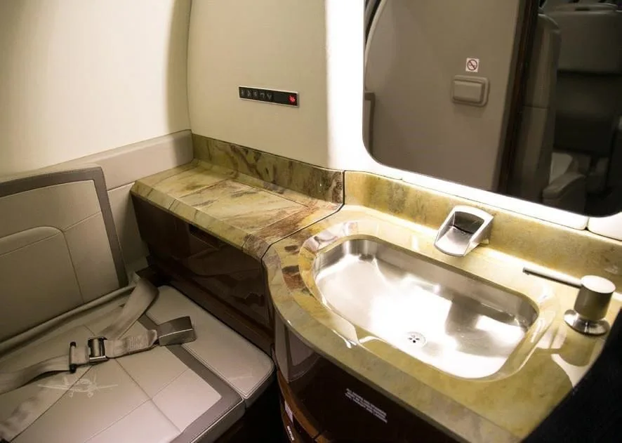 A luxurious aircraft lavatory featuring a sink with a marble-like countertop and a belted seat.