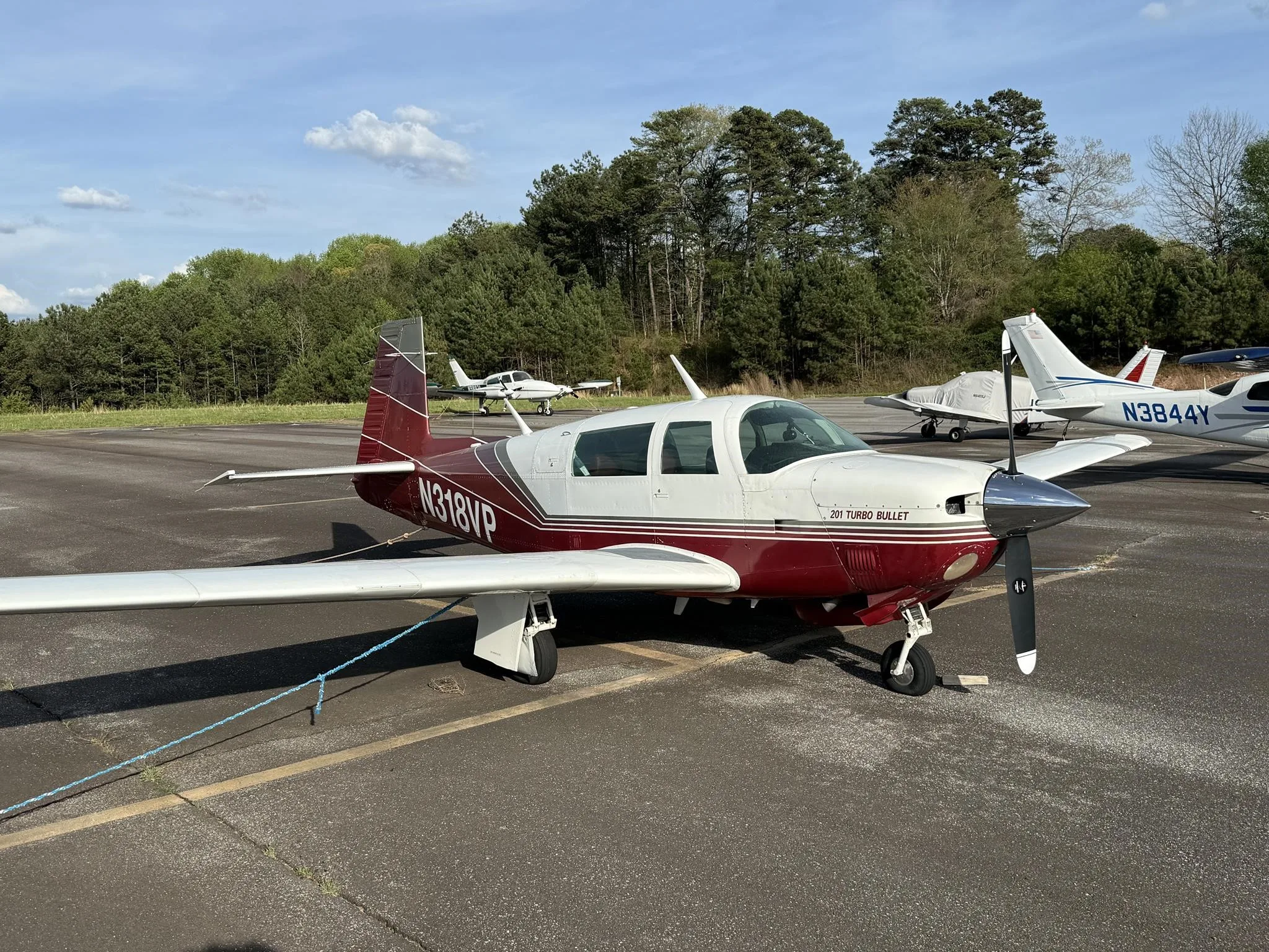 A red and white Mooney 201 Turbo Bullet aircraft, N318VP, parked on an asphalt ramp with other aircraft in the background.