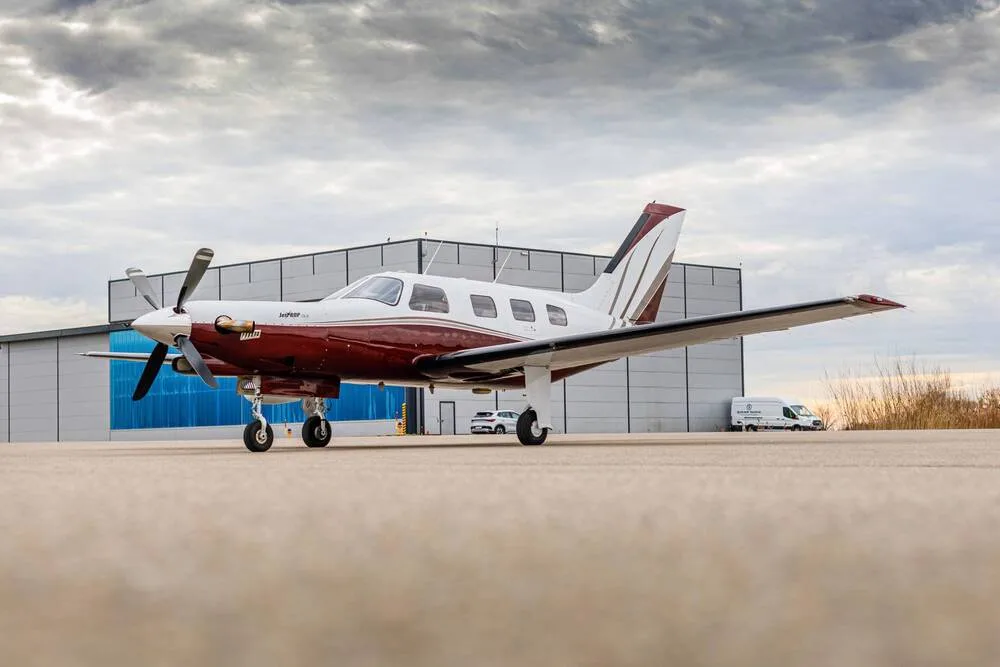 A white and maroon single-engine turboprop aircraft parked on an airfield in front of a hangar.