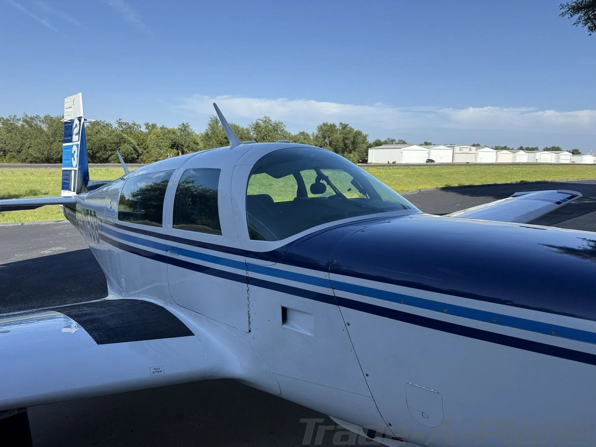A close-up side view of the cockpit and fuselage of the white and blue aircraft, N1156G, with hangars in the distance.