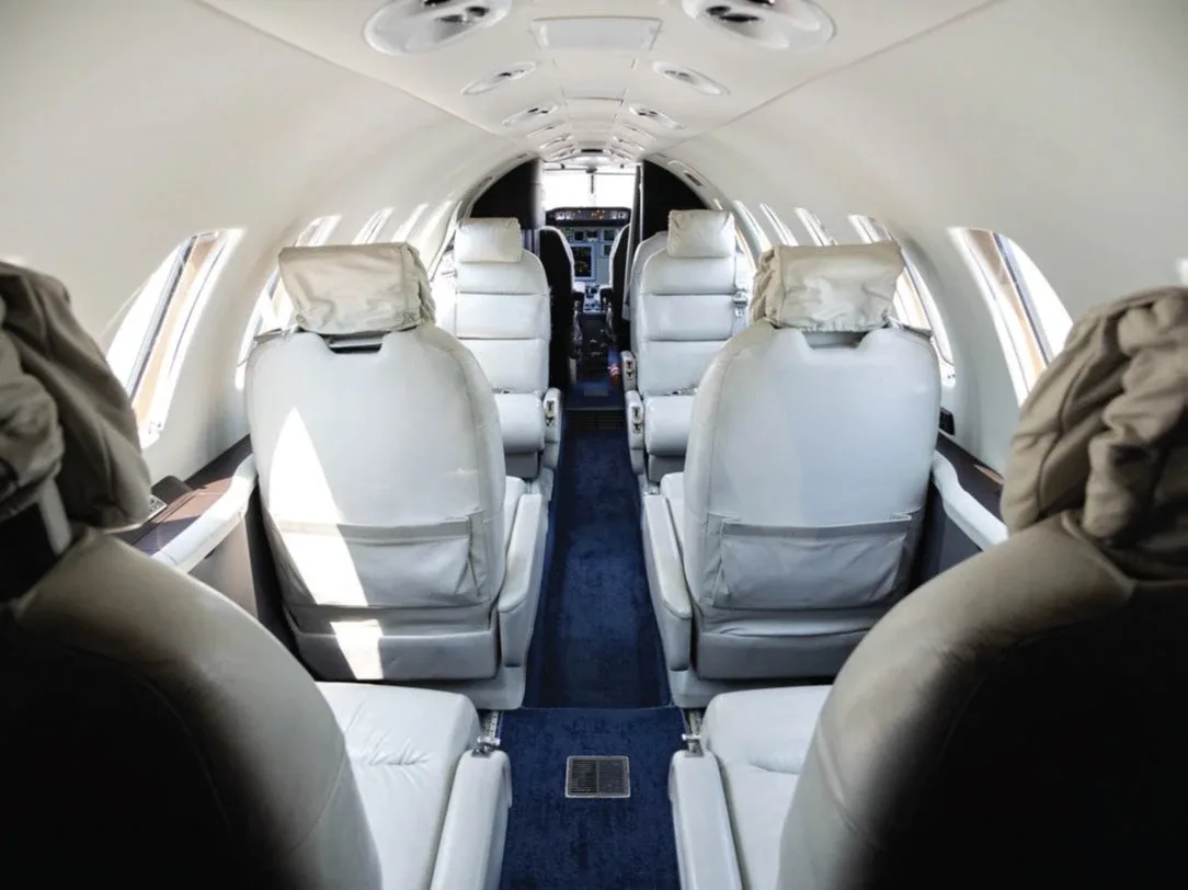 The interior cabin of a business jet features light-colored leather seats and a blue carpet.