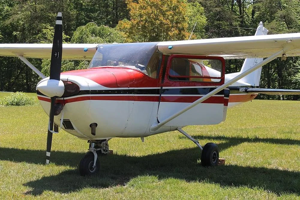 A front-left view of a red and white single-engine propeller aircraft (N6924X) parked on a grassy field.