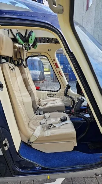 The front cabin seats of a helicopter, showing beige upholstery and some flight controls.