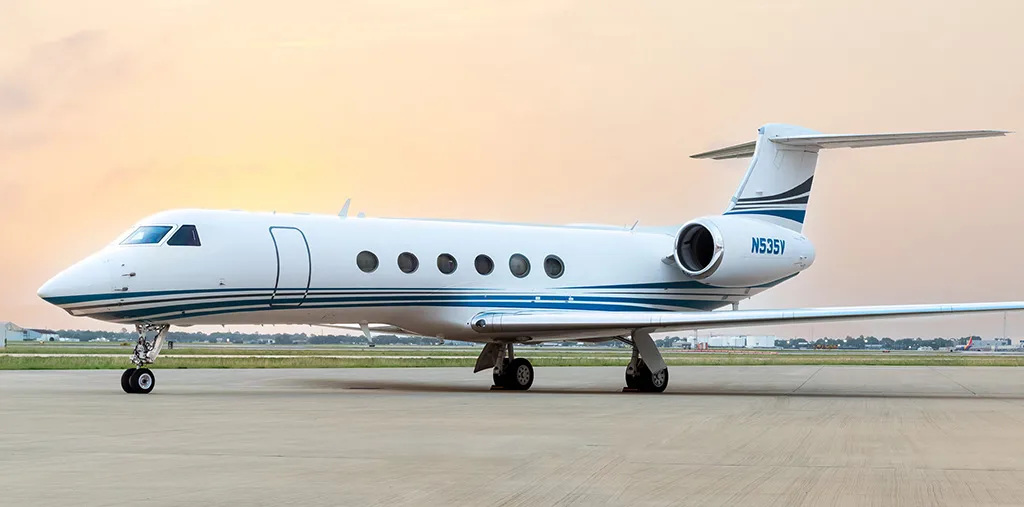 A white Gulfstream G550 business jet with blue stripes on the fuselage, tail number N535V, parked on an airfield.