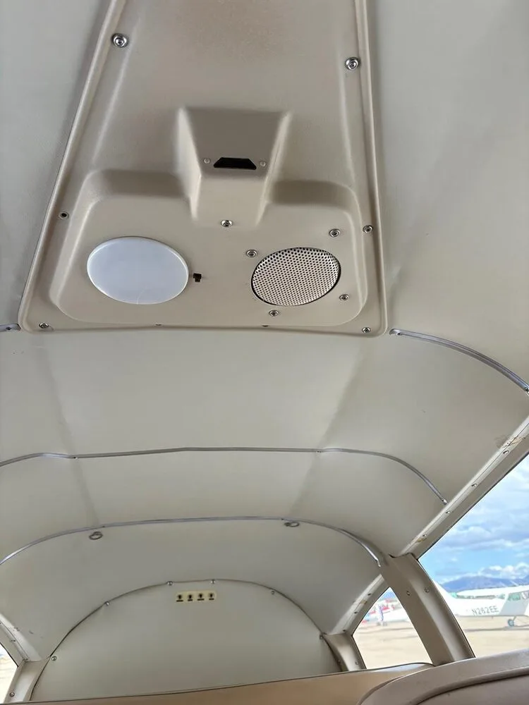 The beige interior ceiling of the aircraft cabin with a light and speaker, and a glimpse of another aircraft outside.