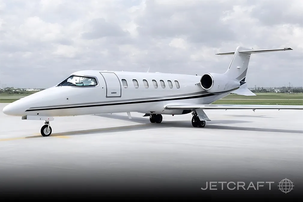 A white business jet with black and grey stripes on the tarmac, viewed from the front-left side.