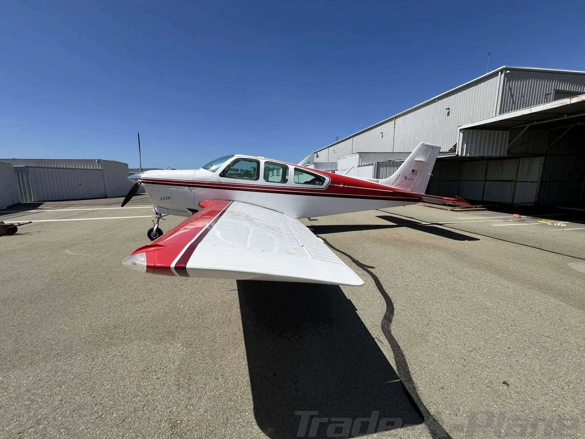 Side view of a white and red Beechcraft Bonanza with a V-tail, parked on an airfield.
