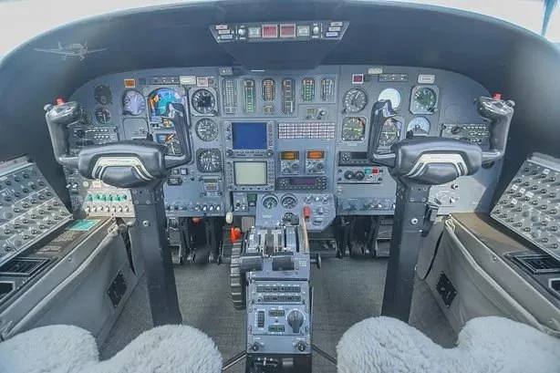 The aircraft cockpit features a complex instrument panel with multiple gauges, screens, and two control yokes.