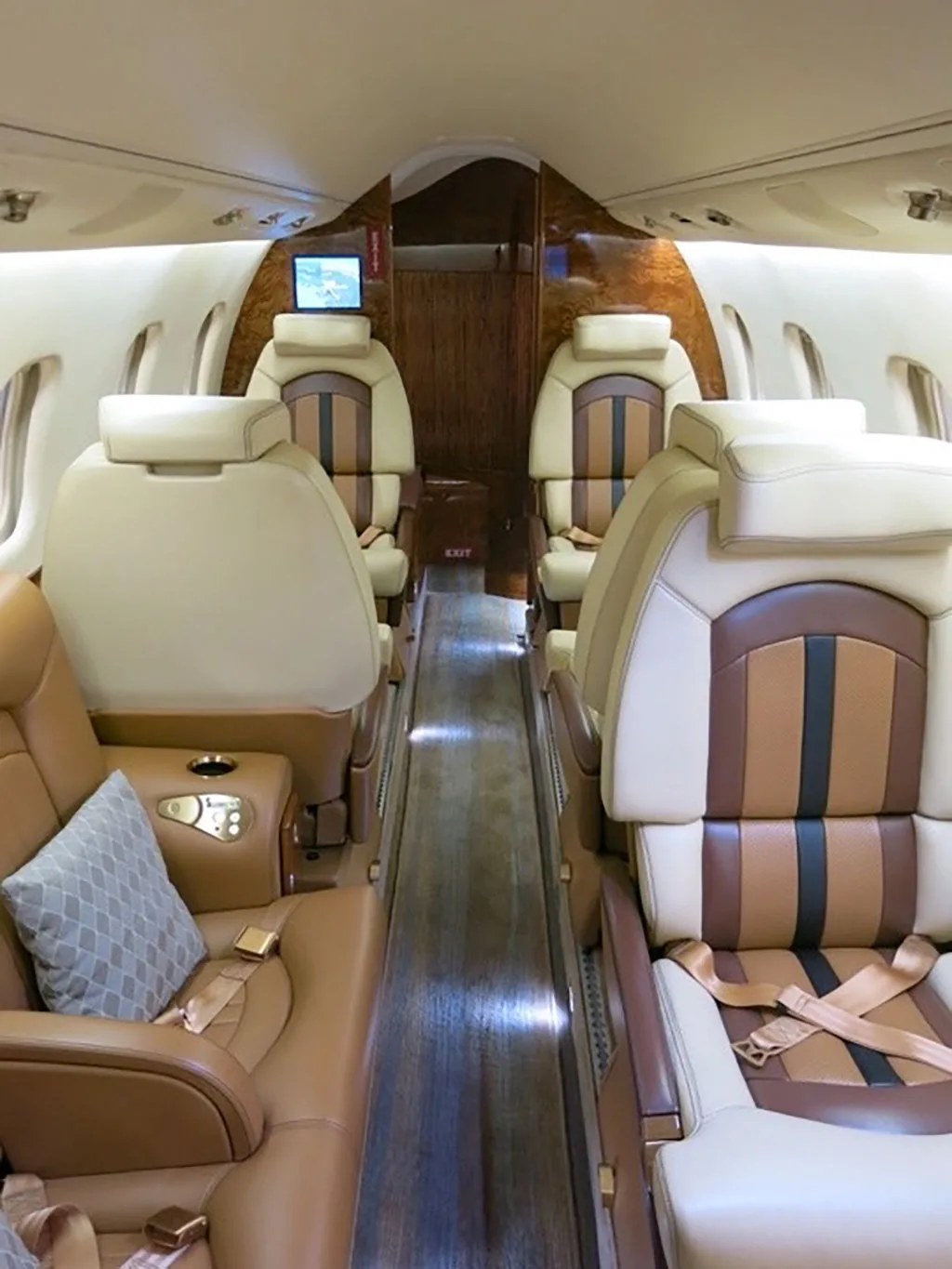 View of the aircraft cabin interior with beige and brown leather seats and a wooden floor, looking forward.