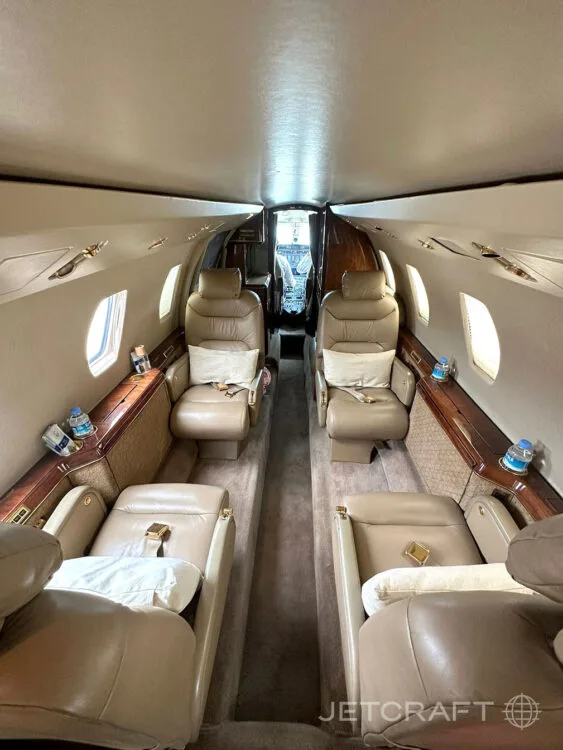 The interior cabin of a business jet, showing tan leather seats and a view towards the cockpit.