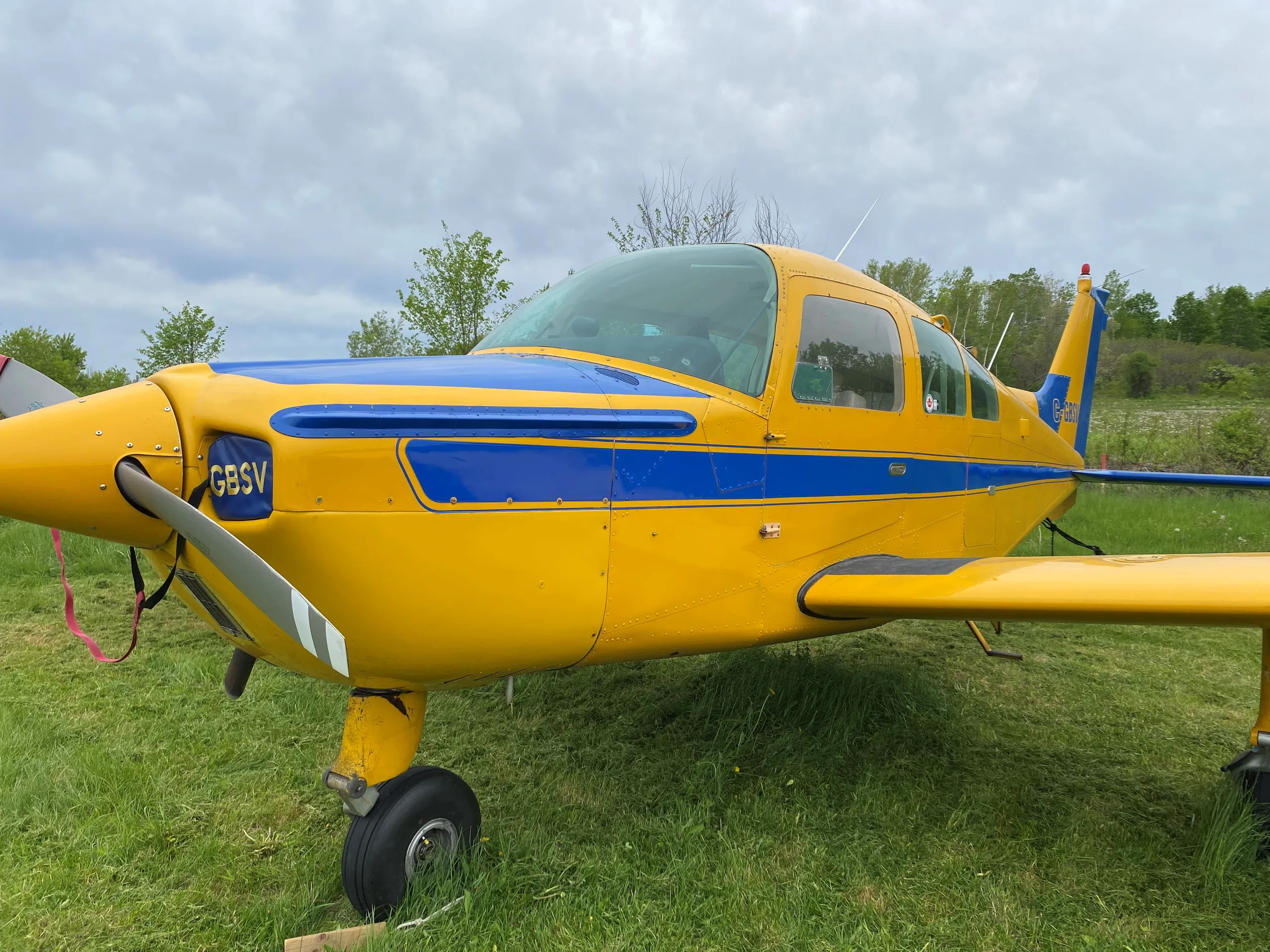 A close-up side view of the front of a yellow and blue single-engine aircraft with registration C-GBSV.