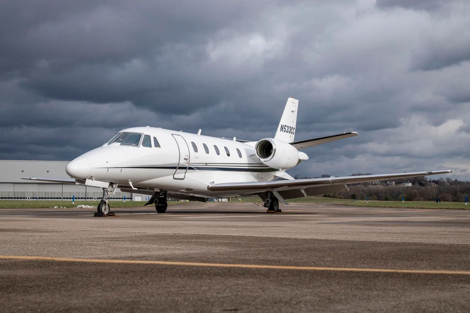 A white business jet with tail number N533CC is parked on an asphalt tarmac under a cloudy sky.