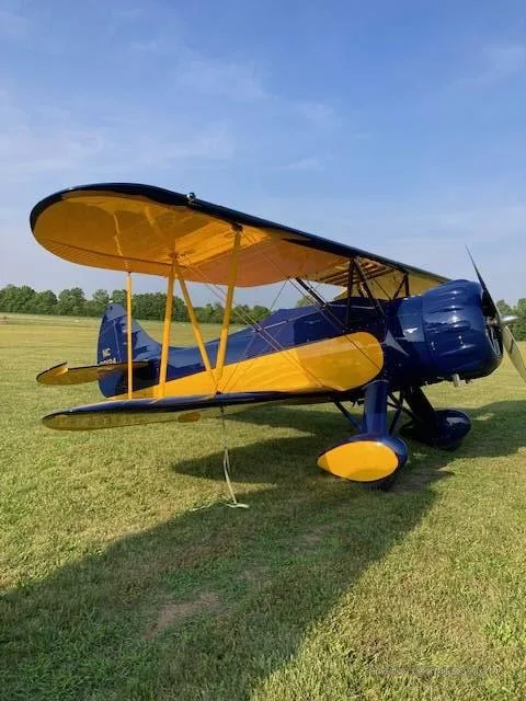 A blue and yellow biplane with registration NC 30124 sits on a green grassy field under a blue sky.