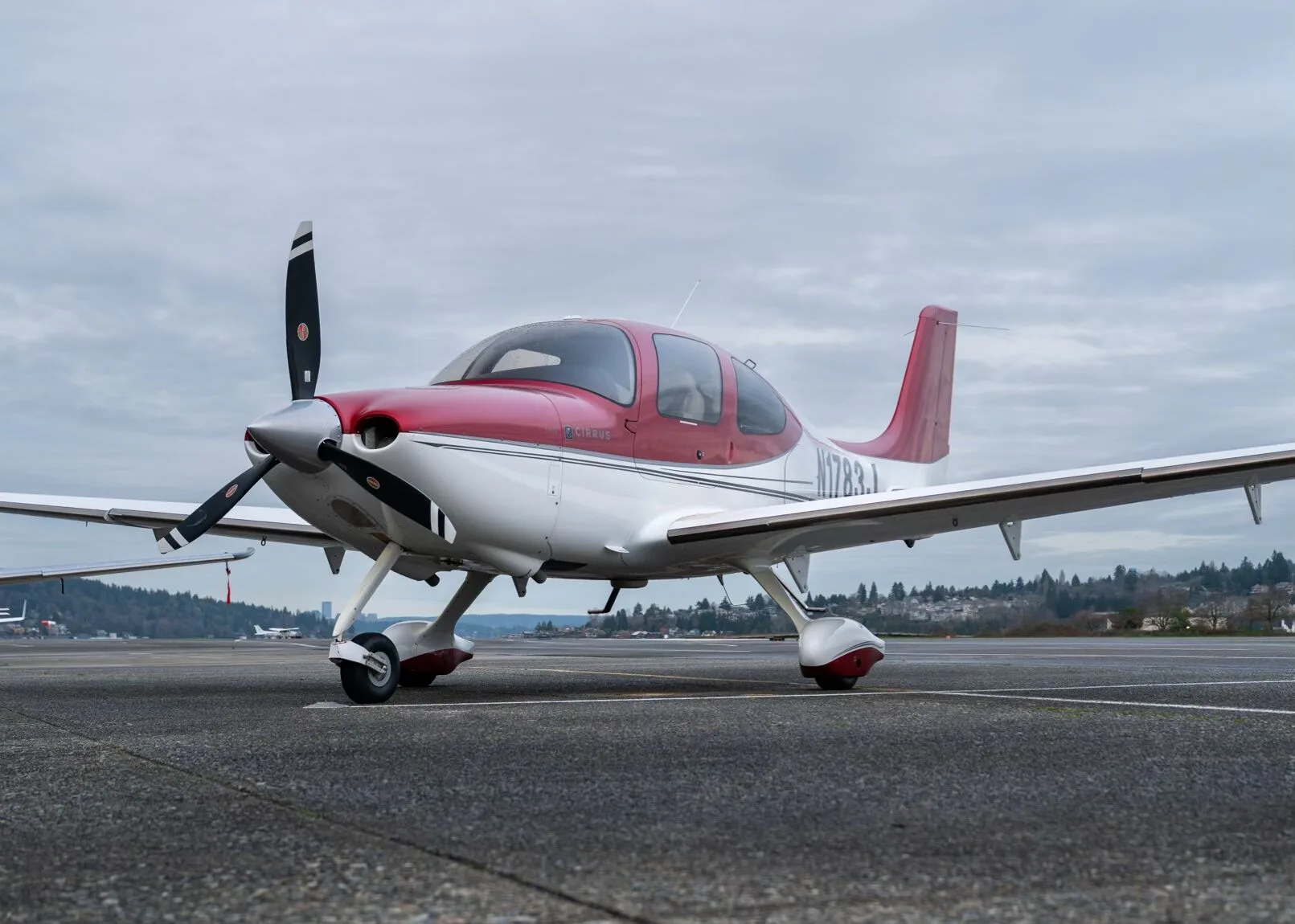 A red and white Cirrus SR22 aircraft, N1783J, parked on a tarmac under a cloudy sky.
