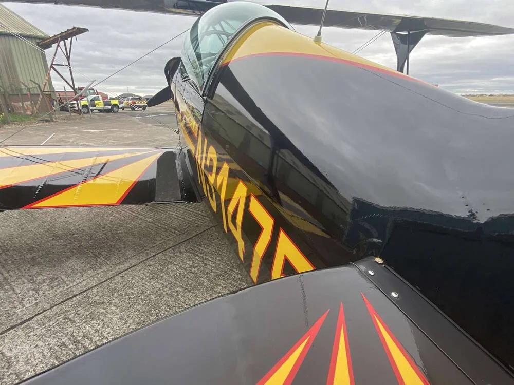 A close-up view of the fuselage and tail section of the black and yellow biplane N31475.