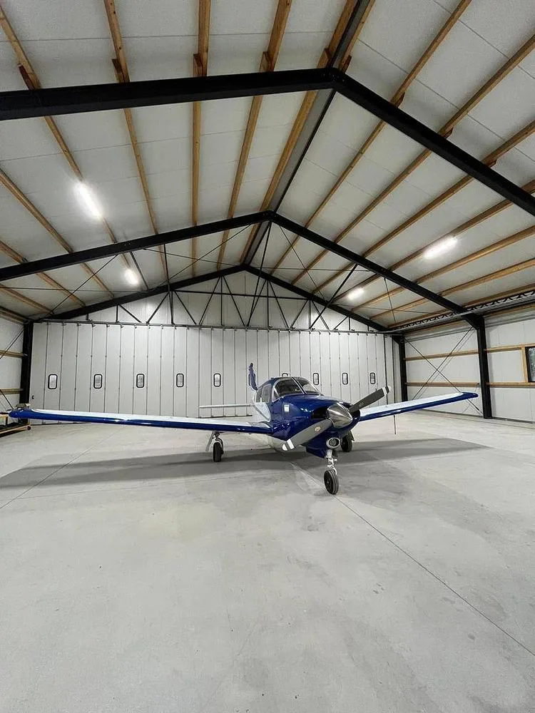 A blue and white single-engine aircraft parked inside a spacious hangar.